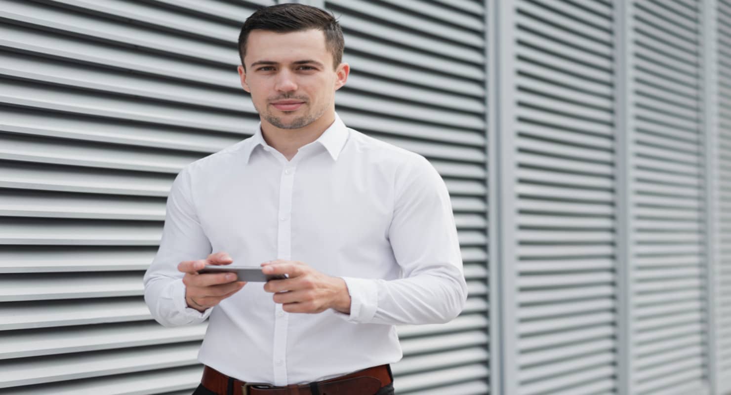 Photo of Man in White Dress Shirt Holding Phone Near Window