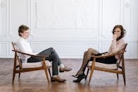 Woman in White Long Sleeve Shirt and Gray Pants Sitting on Brown Wooden Chair